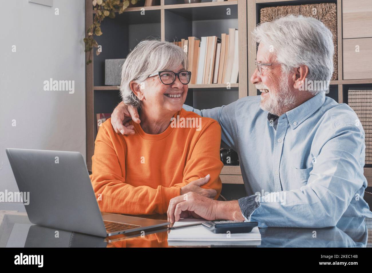 Happy elderly 60s couple sit rest on couch at home pay household