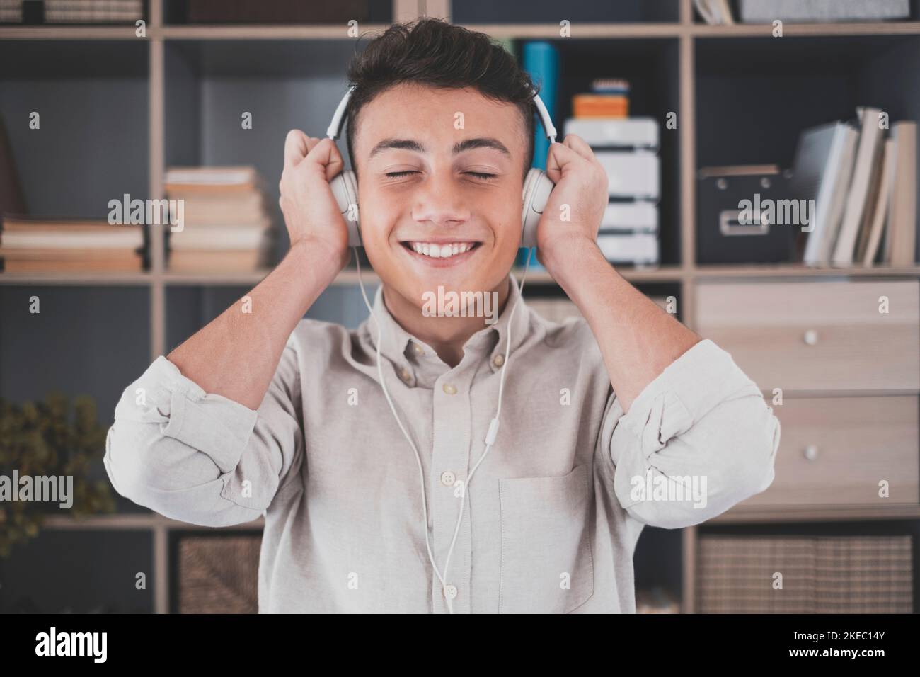 Tranquil carefree young teenager man at home, wearing modern wireless headphones, listening to favorite classic music online, feeling peaceful mindful alone in living room. Stock Photo