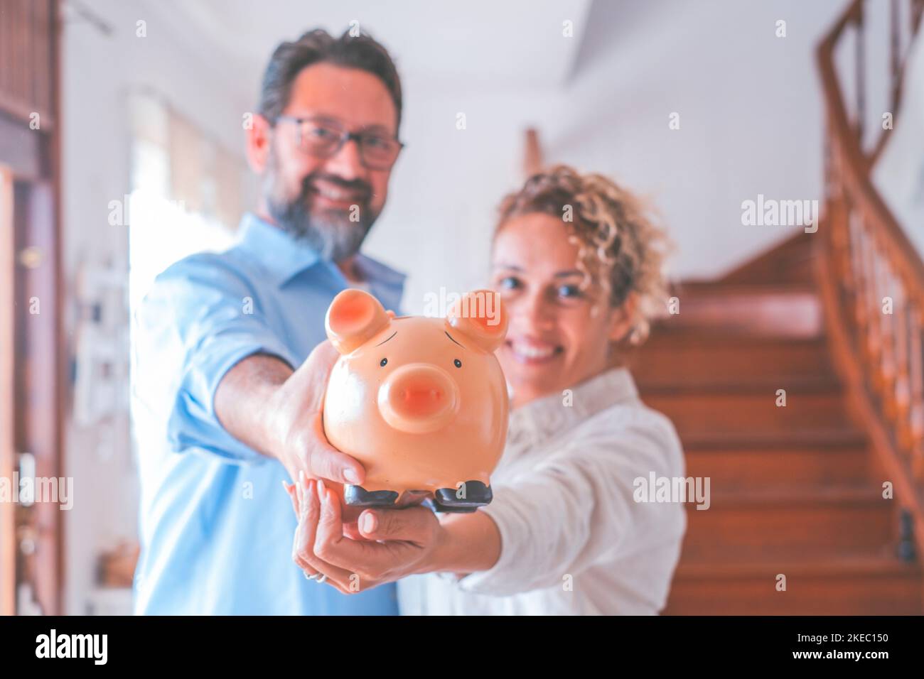 Portrait of happy caucasian couple holding piggy bank to save money to make their future dreams come true. Husband and wife holding piggy bank for savings at home while looking at camera Stock Photo