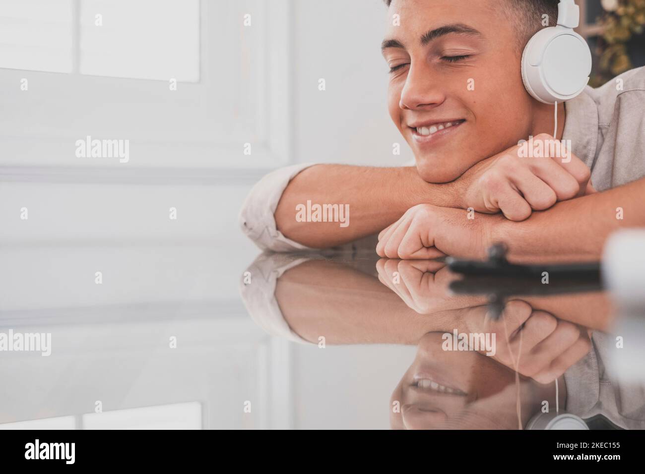 Tranquil carefree young teenager man at home, wearing modern wireless headphones, listening to favorite classic music online, feeling peaceful mindful alone in living room. Stock Photo