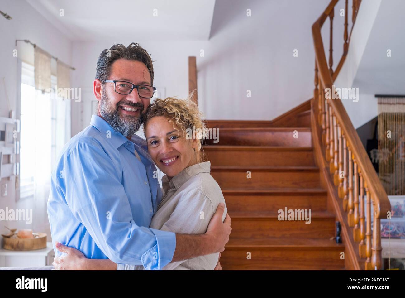 Happy caucasian couple embracing each other in the living room. Loving husband and wife hugging at home. Profile of affectionate man and woman spending leisure time together at modern house Stock Photo