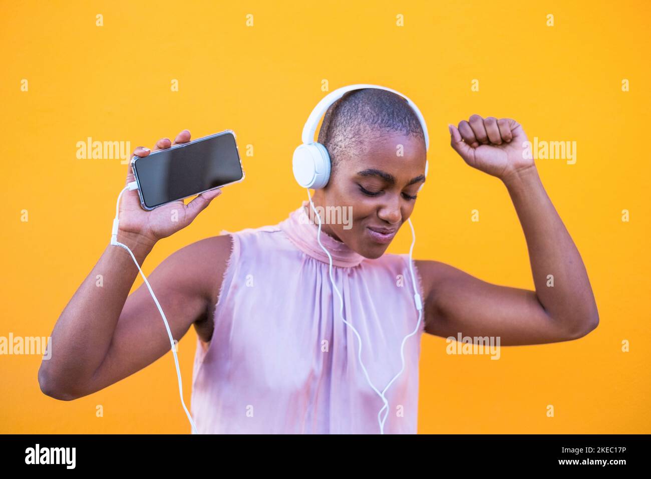 Close up and portrait of beautiful afro American woman smiling and having fun dancing while listening music with headphones from her phone - enjoying using technology lifestyle Stock Photo
