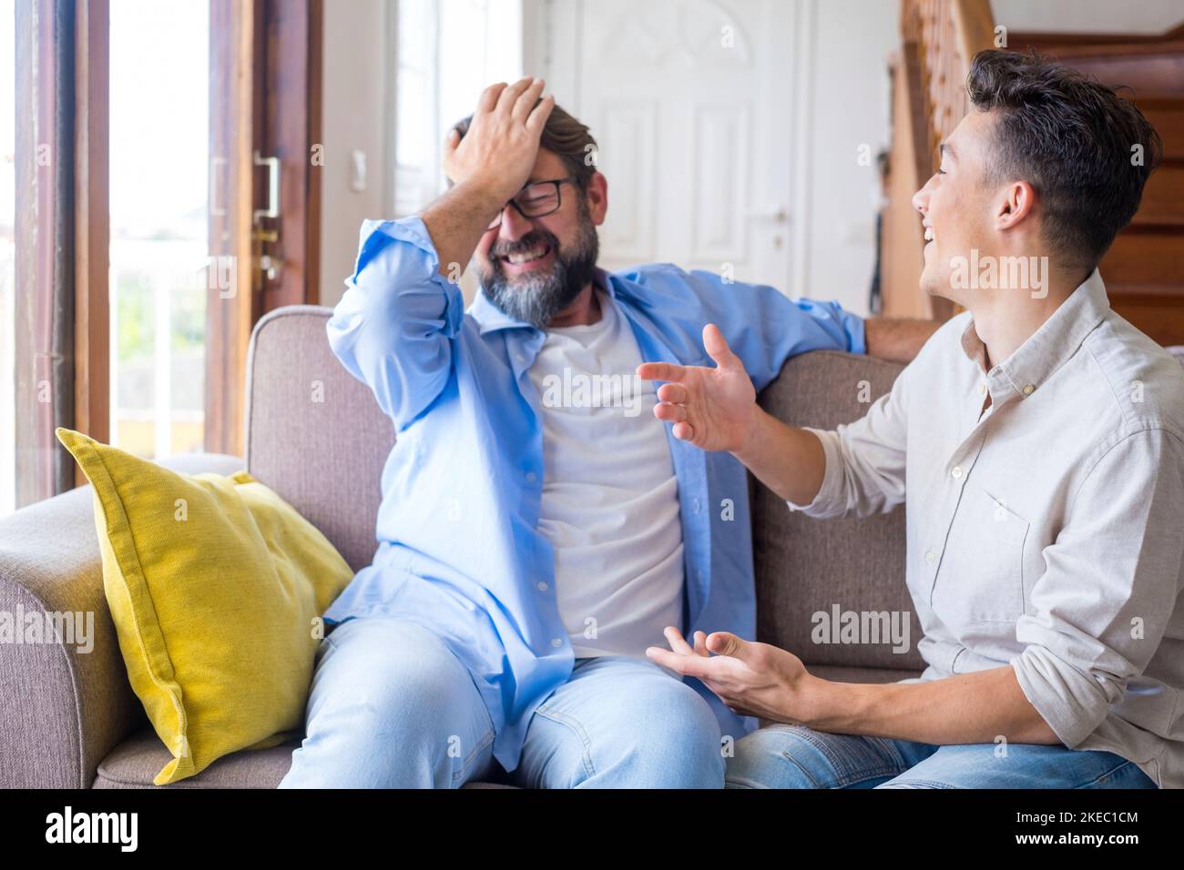 Happy father and son chatting on sofa at home. Cheerful father with teenage son sitting on couch in the living room of apartment. Father and son spending leisure time at home Stock Photo