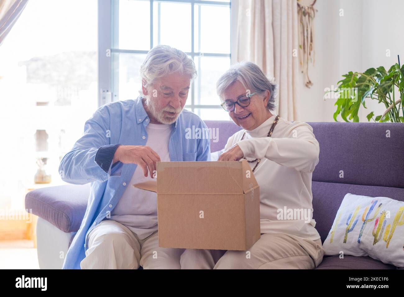 Happy mature aged older family couple unpacking carton box, satisfied with internet store purchase or unexpected gift, feeling excited of fast delivery shipping service, positive shopping experience. Stock Photo