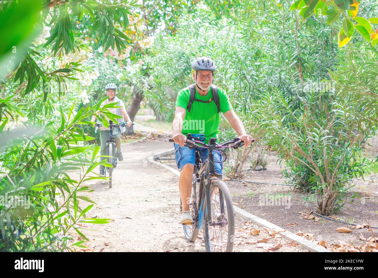 Two happy old mature people enjoying and riding bikes together to be fit and healthy outdoors. Active seniors having fun training in nature. Portrait of one old man smiling in a bike trip with his wife Stock Photo