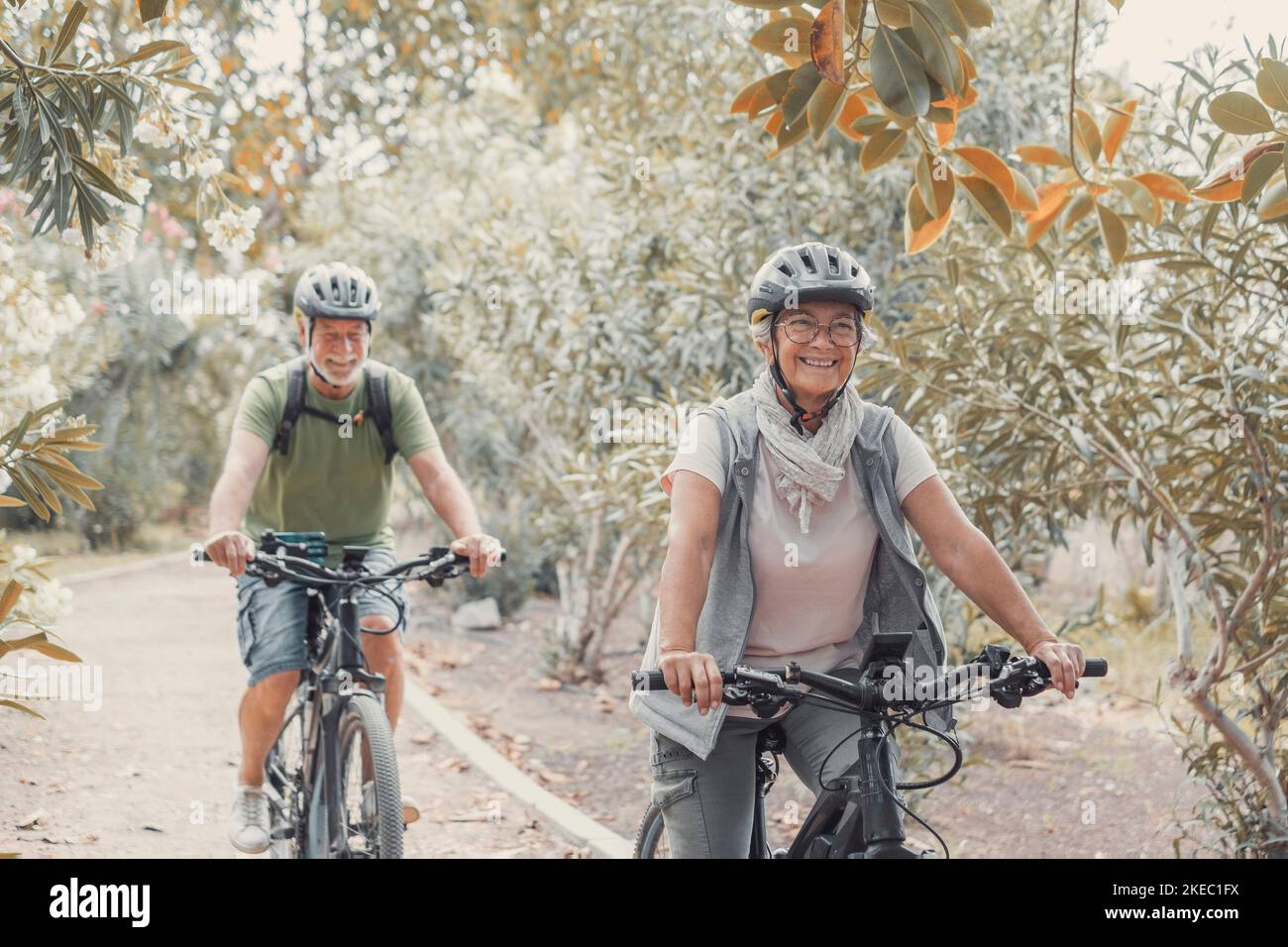 Two happy old mature people enjoying and riding bikes together to be fit and healthy outdoors. Active seniors having fun training in nature. Stock Photo