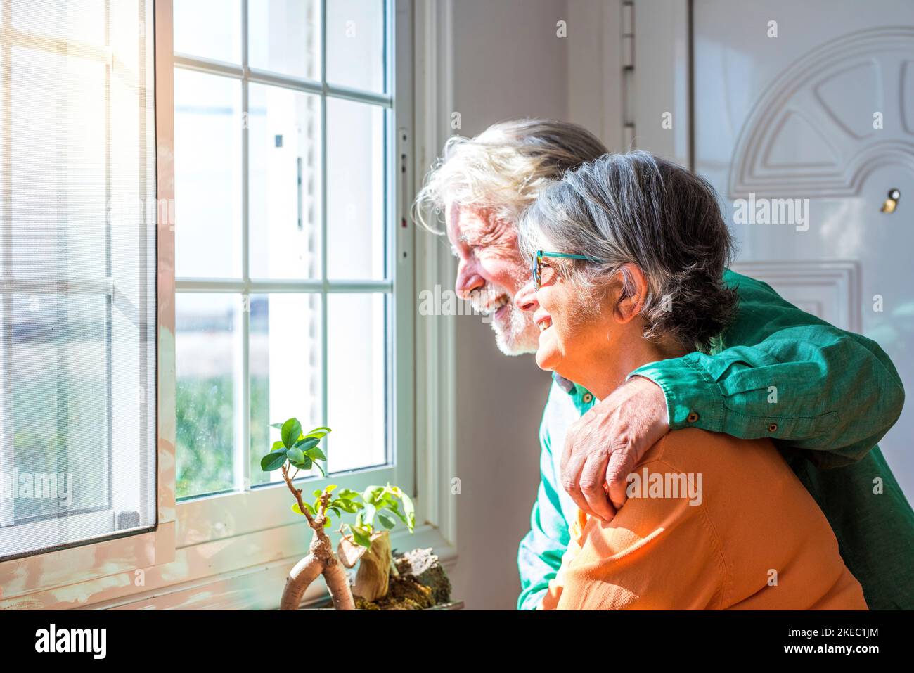 couple of two cute old and mature people or seniors having fun together at home looking outside of their house smiling and laughing Stock Photo