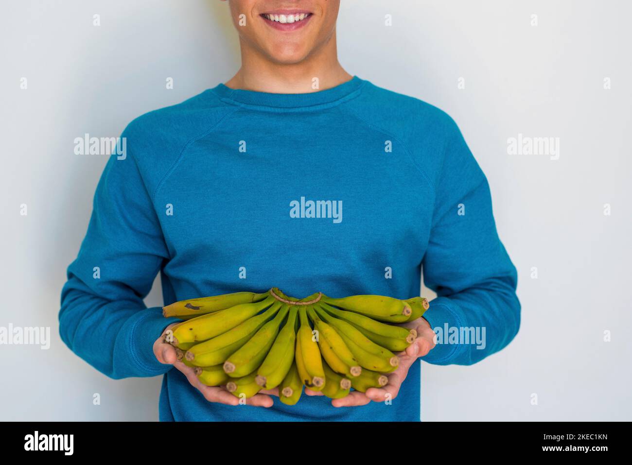 portrait and close up of man or teenager or young boy holding a lot of bananas and smiling looking at the camera - holding fruit - healthy lifestyle and concept and properties of banana Stock Photo
