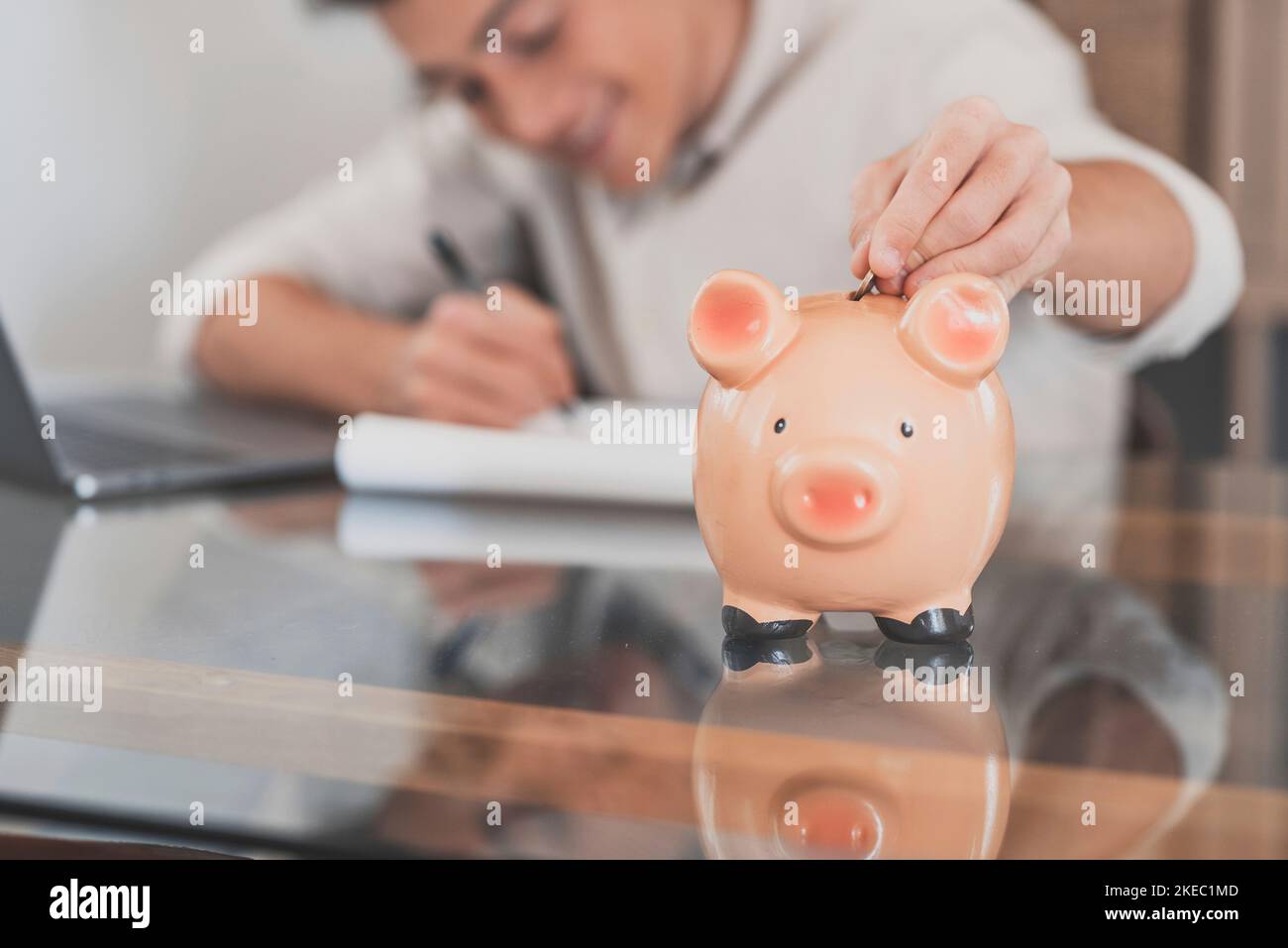 Man sit at desk manage expenses, calculate expenditures, pay bills online use laptop, makes household finances analysis, close up focus on pink piggy bank. Save money for future, be provident concept Stock Photo