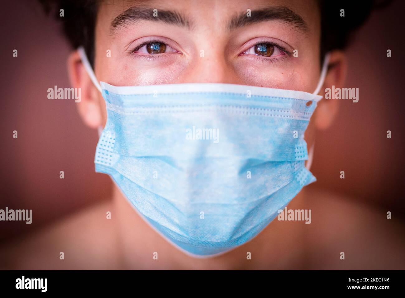 close up and portrait of one millennial teenager man looking at the camera sad wearing mask and crying for the covid-19 Stock Photo