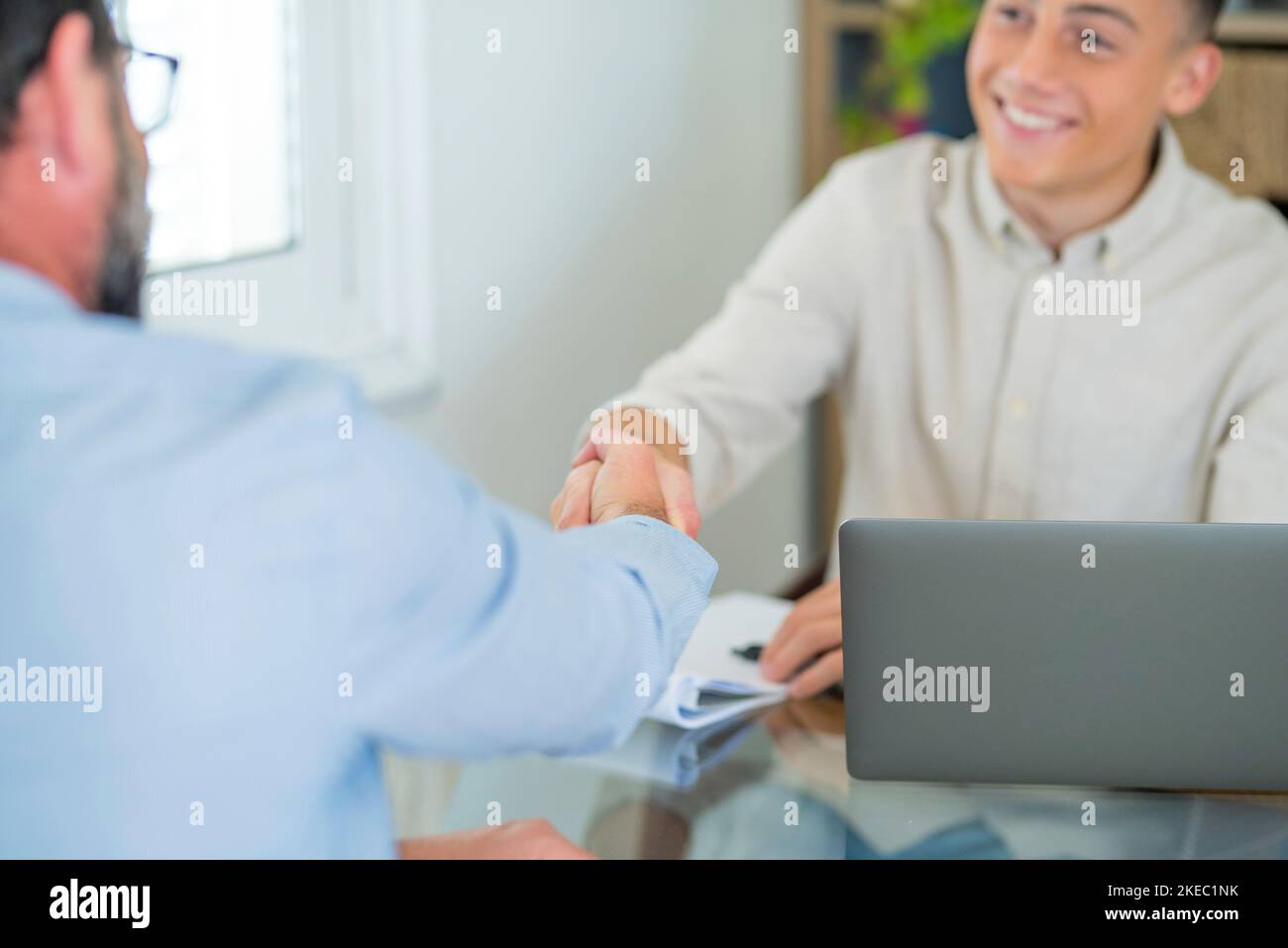 Smiling caucasian teenager hr manager handshake hire male candidate at job interview make good first impression, happy cheerful young client shake hand of bank broker, respect, business agreement concept Stock Photo