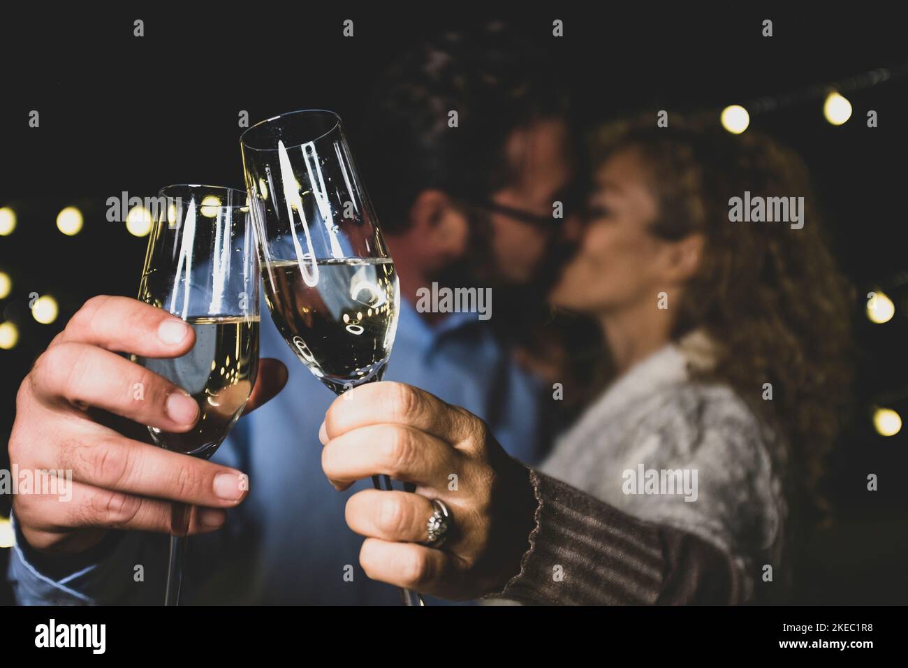 Affectionate caucasian couple kissing each other while toasting champagne glasses celebrating new year party. Loving husband and wife kissing each other while partying with white wine glasses in hands Stock Photo