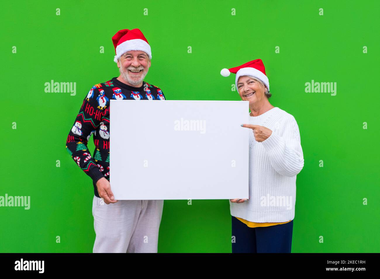 portrait of couple of two happy seniors wearing christmas clothes and holding a big white sheet with copy space to write your text here Stock Photo
