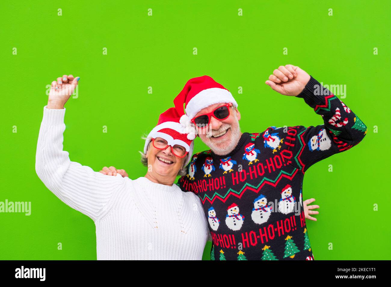 portrait of couple of two seniors and mature and old people having fun enjoying christmas day together wearing christmas clothes and with green colorful background Stock Photo