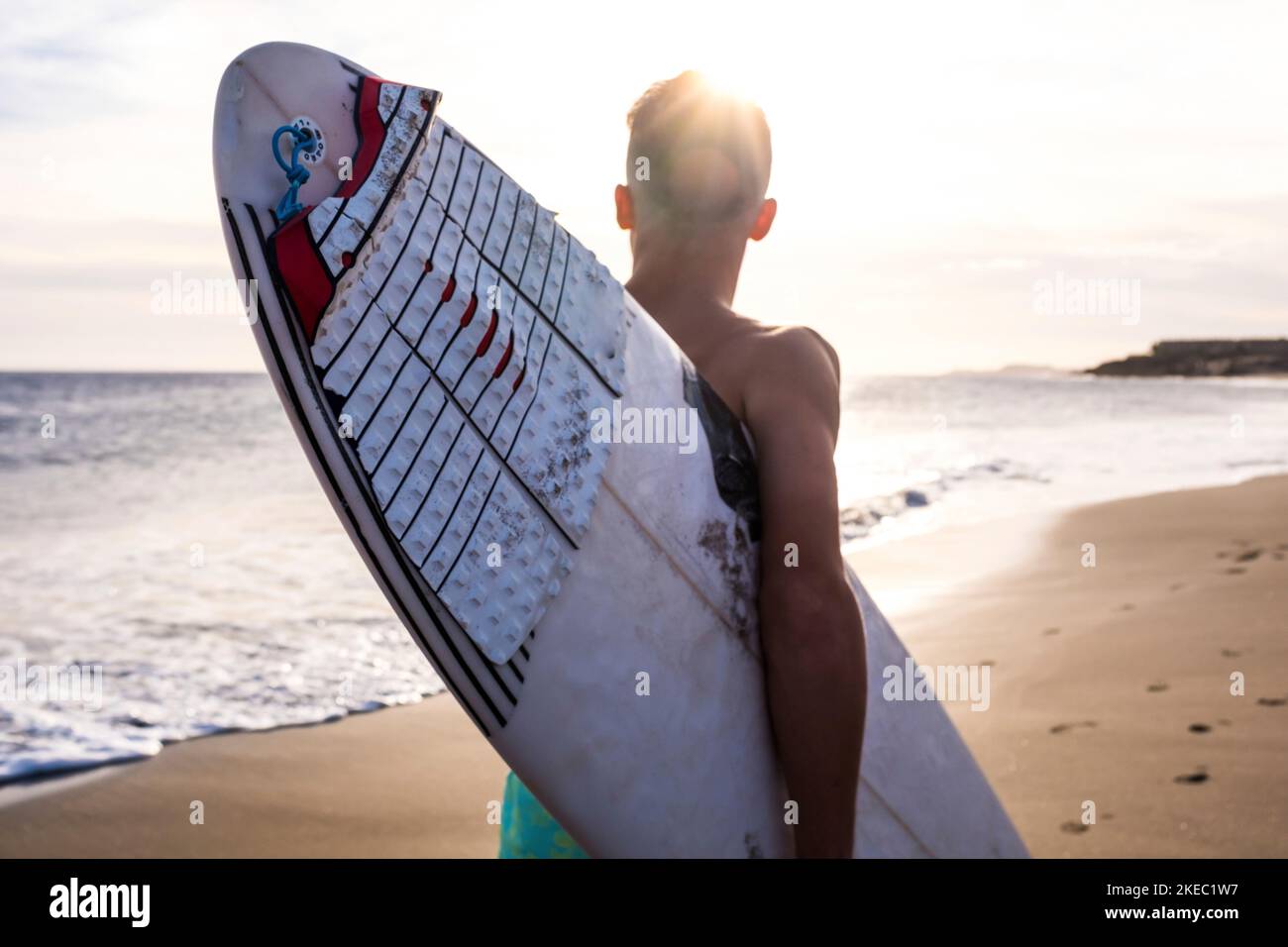 close up of man running on the beach with his surfboard going surfing at summer with the sunset Stock Photo