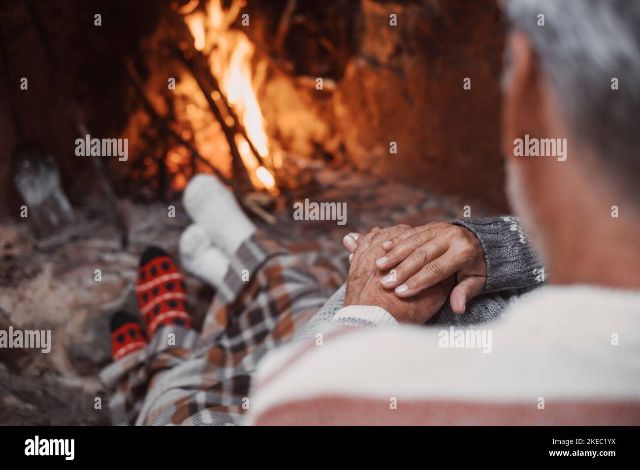 Old caucasian couple spending leisure time together at home. Loving romantic husband and wife relaxing while holding hands in front of burning fireplace during winter christmas holiday Stock Photo