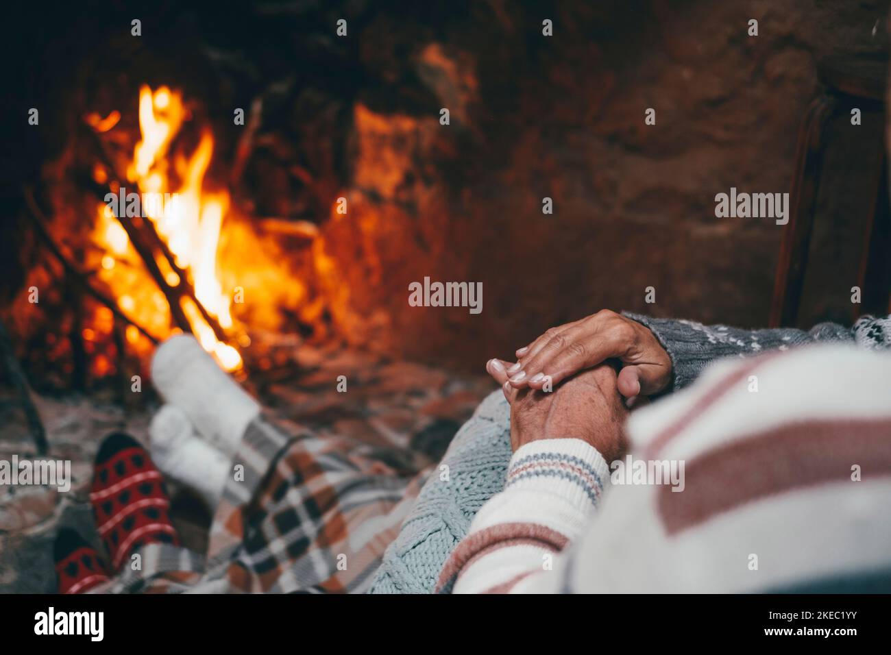 Old caucasian couple spending leisure time together at home. Loving romantic husband and wife relaxing while holding hands in front of burning fireplace during winter christmas holiday Stock Photo