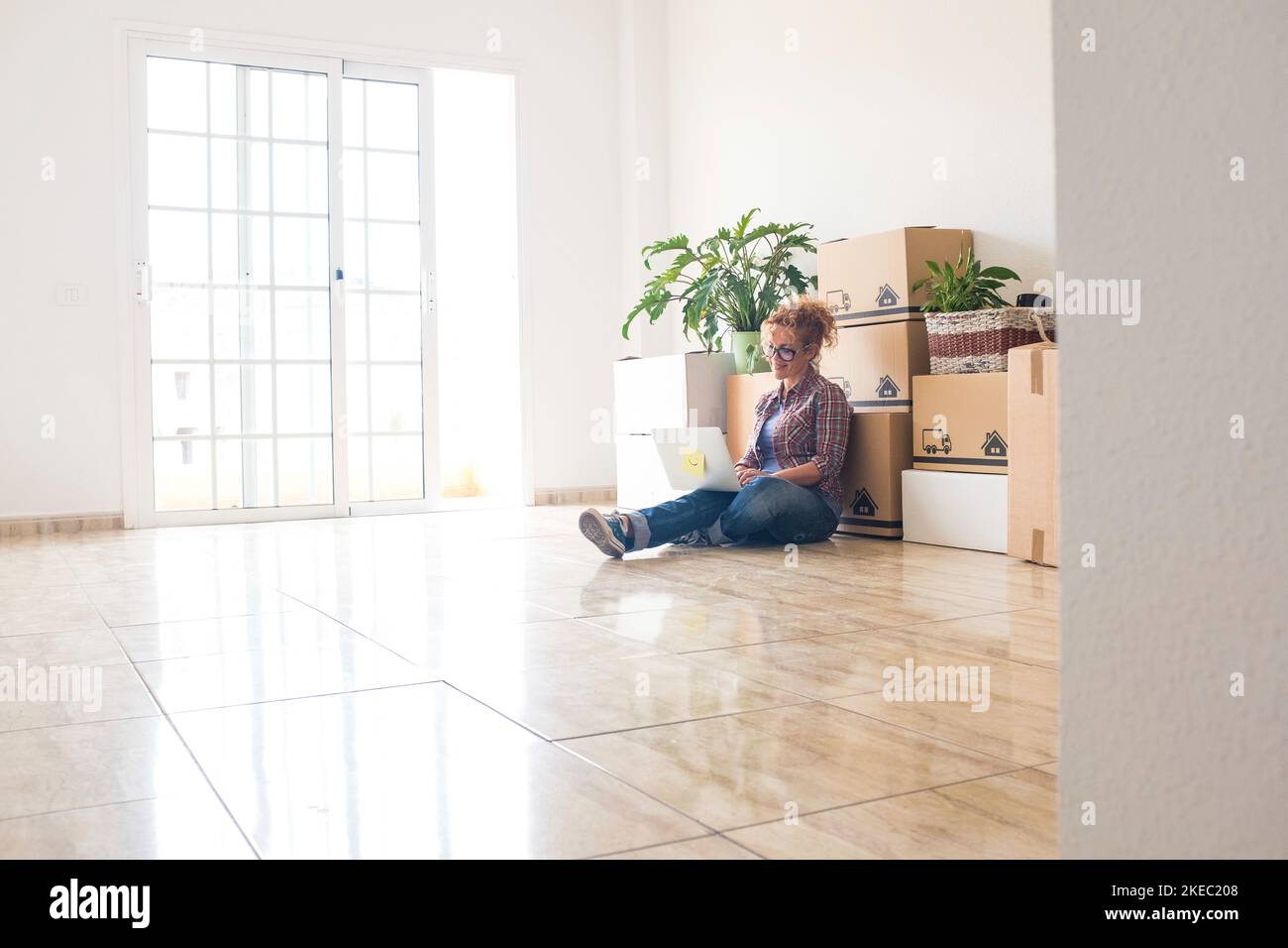 one young beautiful woman using her laptop or computer pc in a empty new house with boxes and packs on her back - independent lifestyle choosing to go live alone with a new home Stock Photo