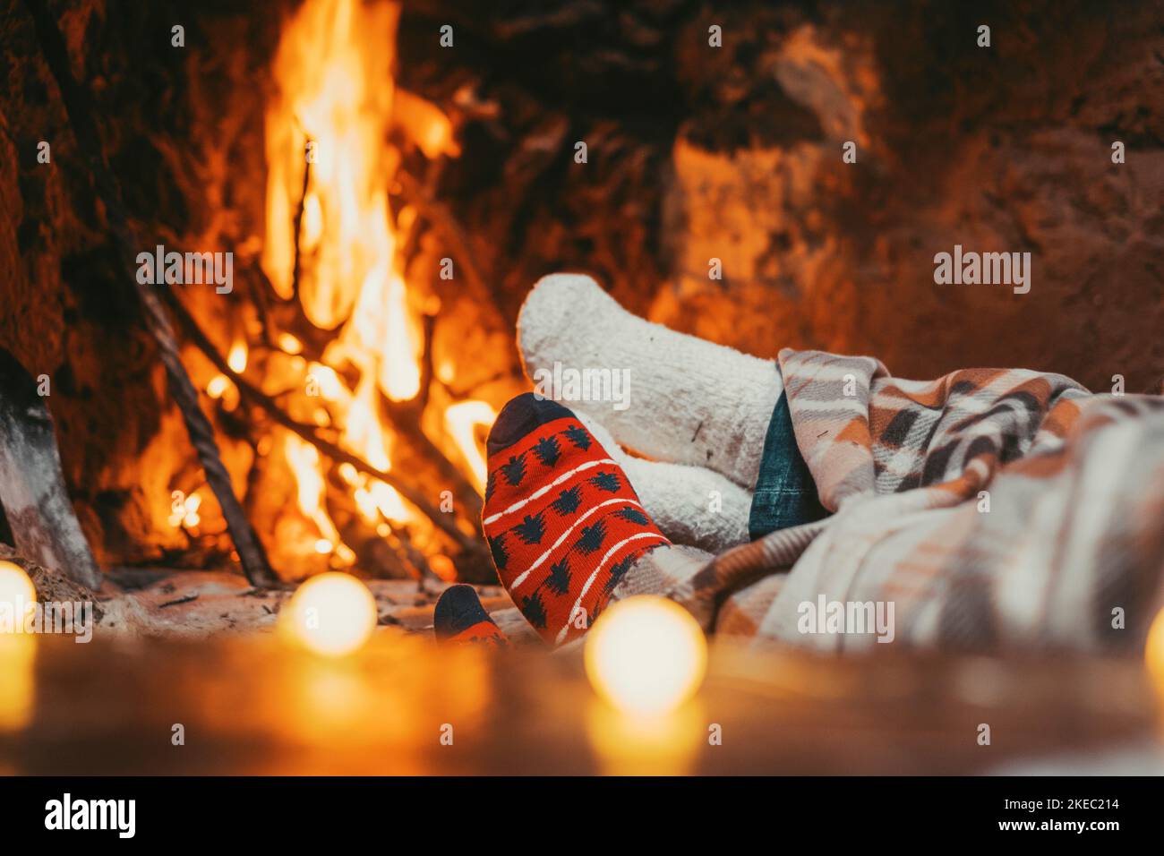 Low section legs of husband and wife covered in socks and warm blanket relaxing in front of burning fireplace during winter christmas holiday. Pair of feet in woollen socks by the Christmas fireplace Stock Photo