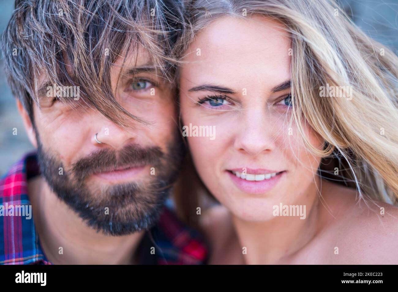 close up and portrait of beautiful and handsome man and woman togethe with their faces near each other looking at the camera smiling - blone woman with blue eyes and handsome man with green eyes Stock Photo