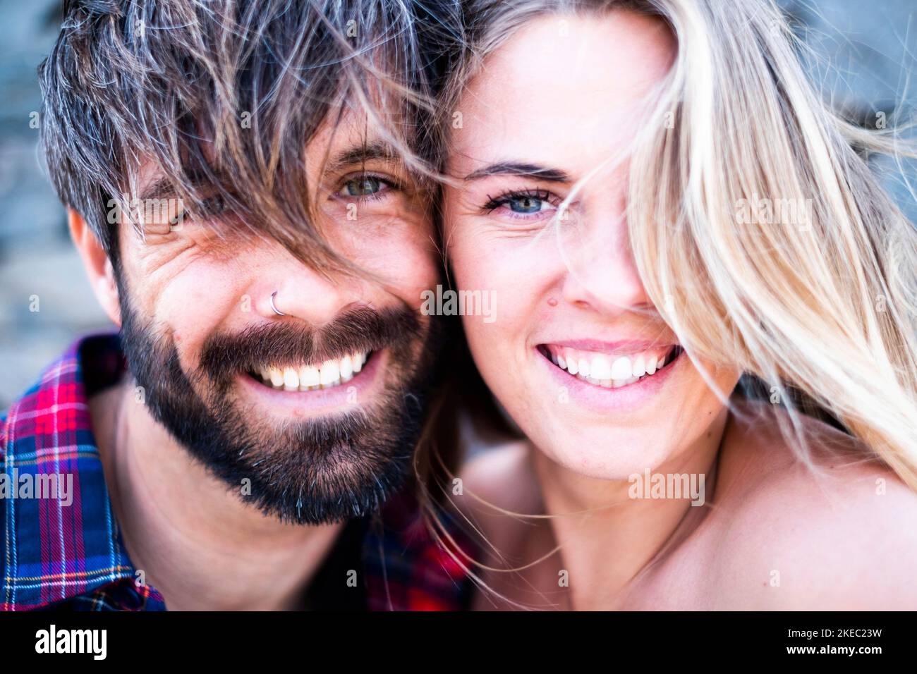 close up and portrait of beautiful and handsome man and woman togethe with their faces near each other looking at the camera smiling - blone woman with blue eyes and handsome man with green eyes Stock Photo