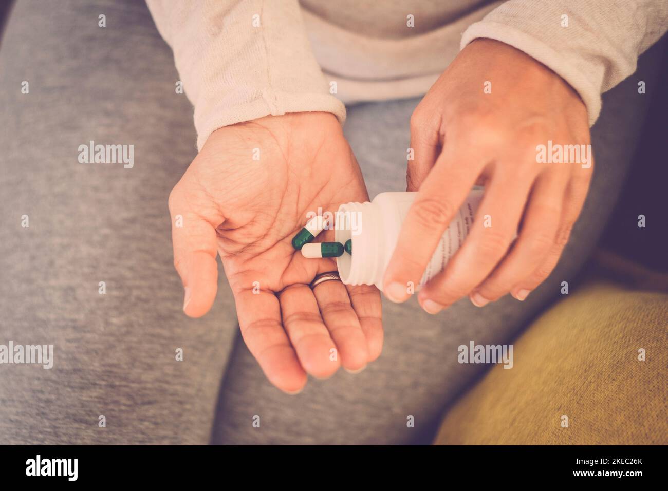 Close up of couple of two hands of woman taking pills and medicaments alone and isolated at home on the sofa. Stock Photo