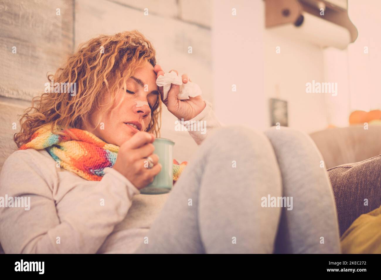 sick and unwell young woman feeling wrong with flu and some virus on the sofa at home. Female with fever and headache feeling wrong indoor alone and isolated. Stock Photo