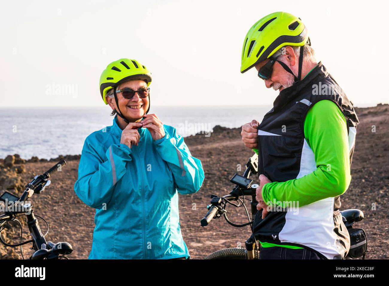 beautiful couple of two seniors riding their bikes together at the rocky beach - active and fitness lifestyle concept - mature woman looking smiling her husband Stock Photo