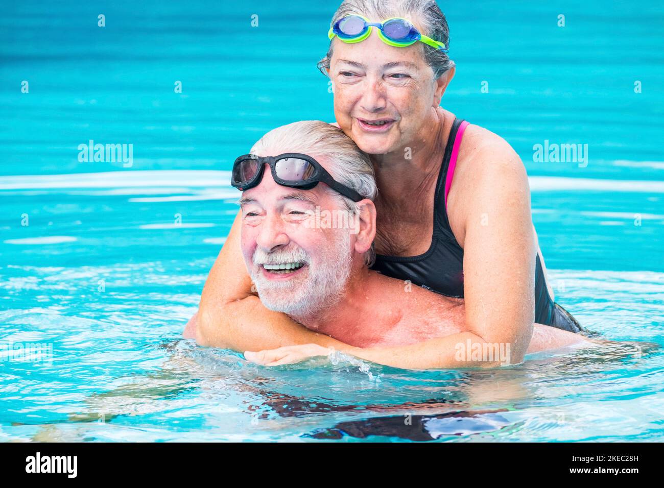 two pensioners or mature old people enjoying summer and vacations in the swimming pool together having fun smiling and laughing - couple of cute seniors in love - happy lifestyle and healthy concept Stock Photo