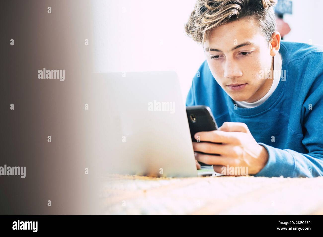 teenager or young man using phone at home on the sofa or on the bed alone having fun and enjoying. Millennial surfing the net with laptop and smartphone and with technologic device Stock Photo
