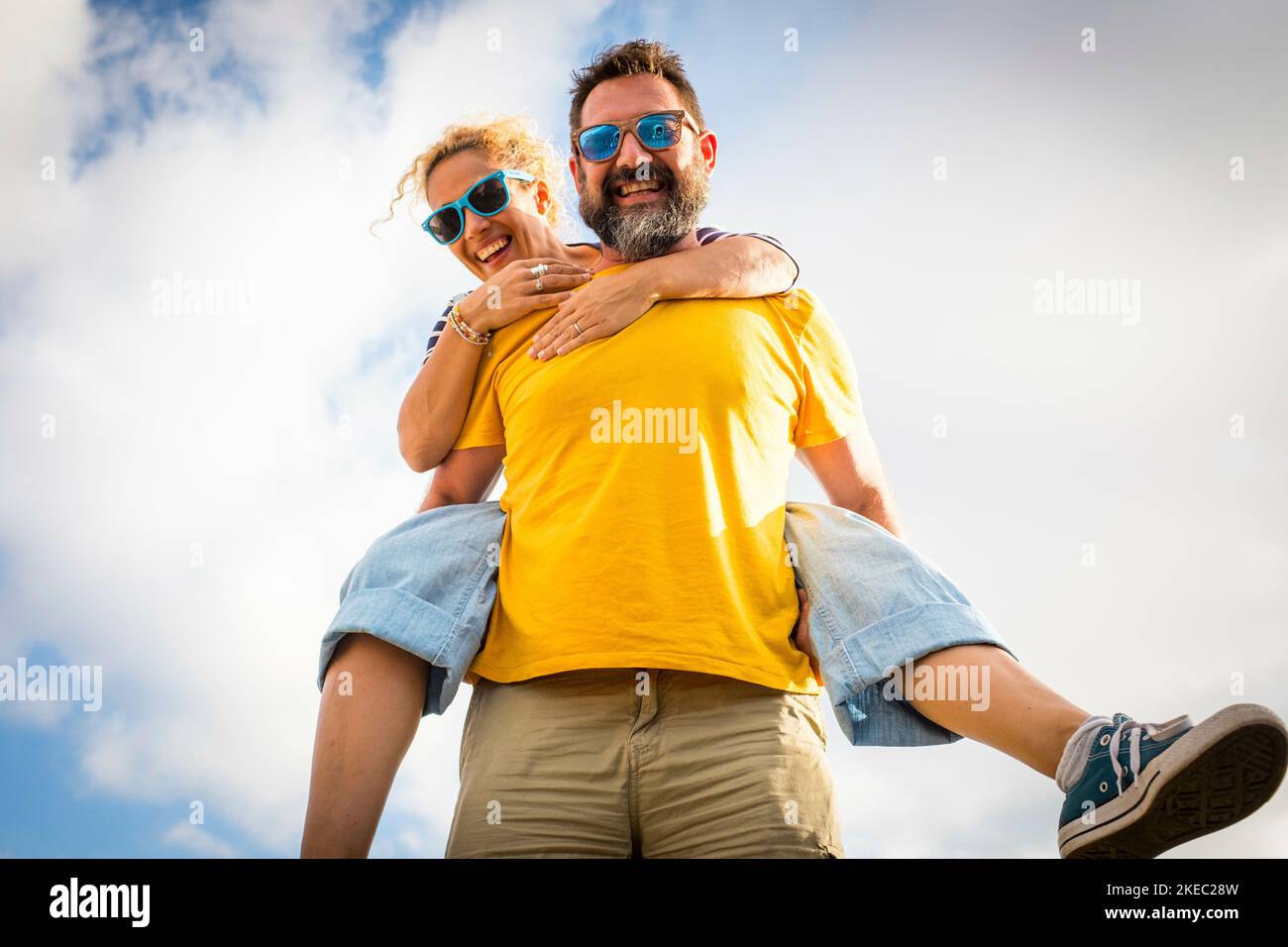 beautiful and cute couple of two adults together having fun and enjoying smiling and looking at the camera - ground view - man carriyng his wife Stock Photo