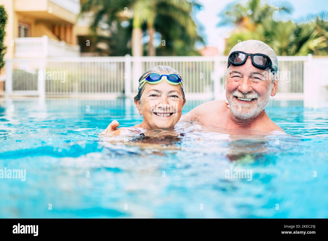 couple of cute seniors and pensioners in the water of the pool having fun and enjoying together - two mature people in love looking at the camera - doing exercise and training together smiling Stock Photo