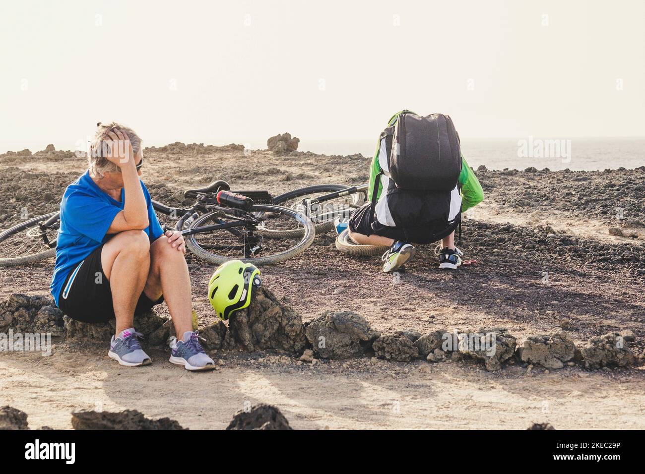 two seniors and pensioners having a problem in the hiull near to the beach - tired woman waiting to her husband fixing up her bike Stock Photo