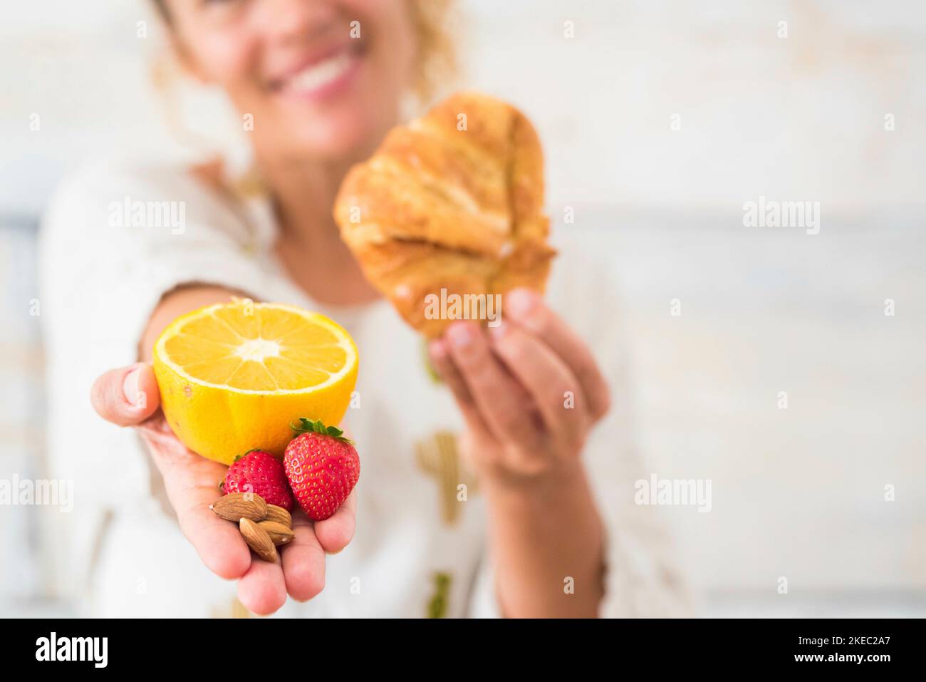 close up of hand of woman holding an orange and strawbberry and in the oter hand a croissant - dieting and healty lifestyle and concept Stock Photo