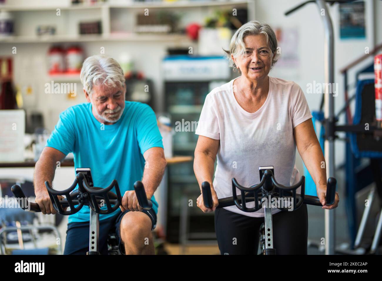 couple of mature people or active seniors doing exercise in the gym riding the bicycle indoor to be healthy - two happy retired with healthy lifestyle Stock Photo