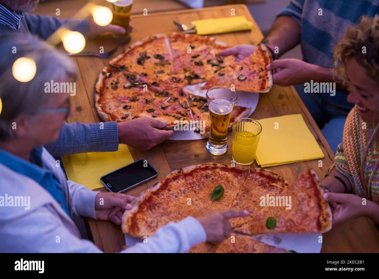 group of four poeple eating pizza and drinking beer together at night at home or in a restaurant - family together celebrating something Stock Photo