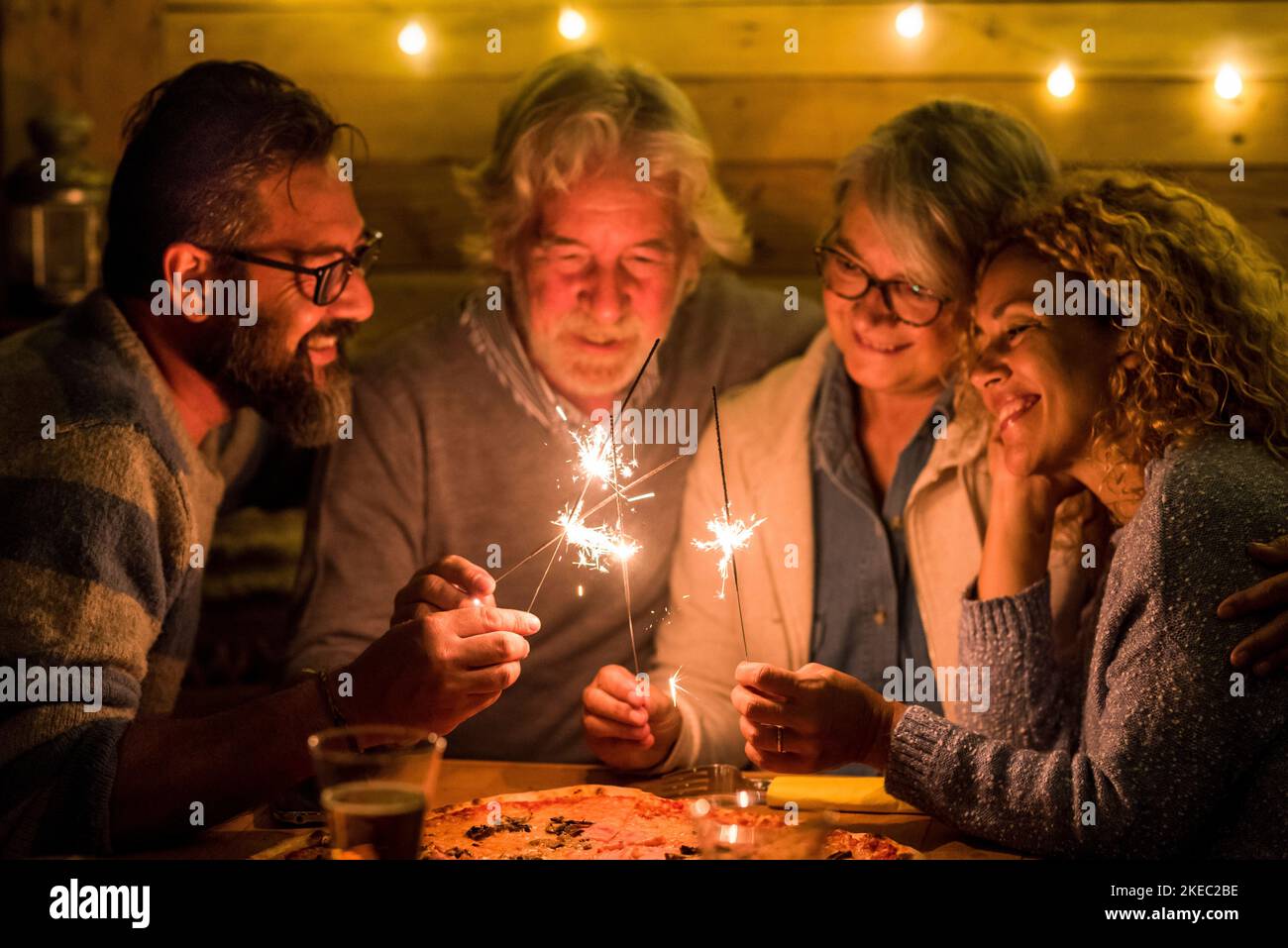group of people celebrating the 2021 new year after a hard 2020 - bye 2020 concept - family enjoying and having fun together with sparklers at home eating pizza at dinner - christimas concept Stock Photo