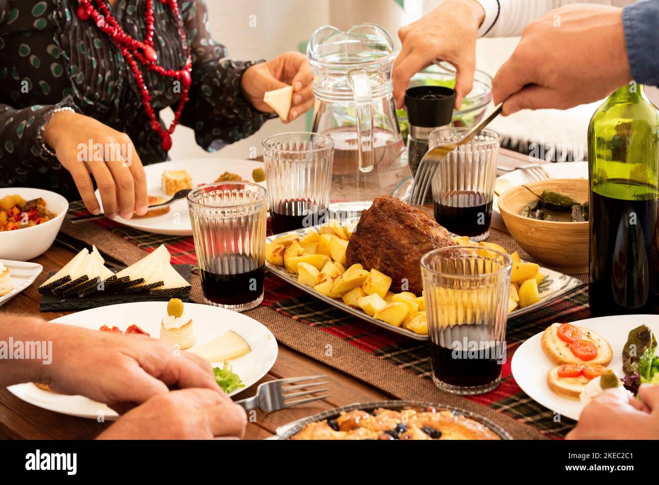 group of four people eating and drinking together at home - celerbating something with chicken and wine - hands taking food from the middle of the table Stock Photo
