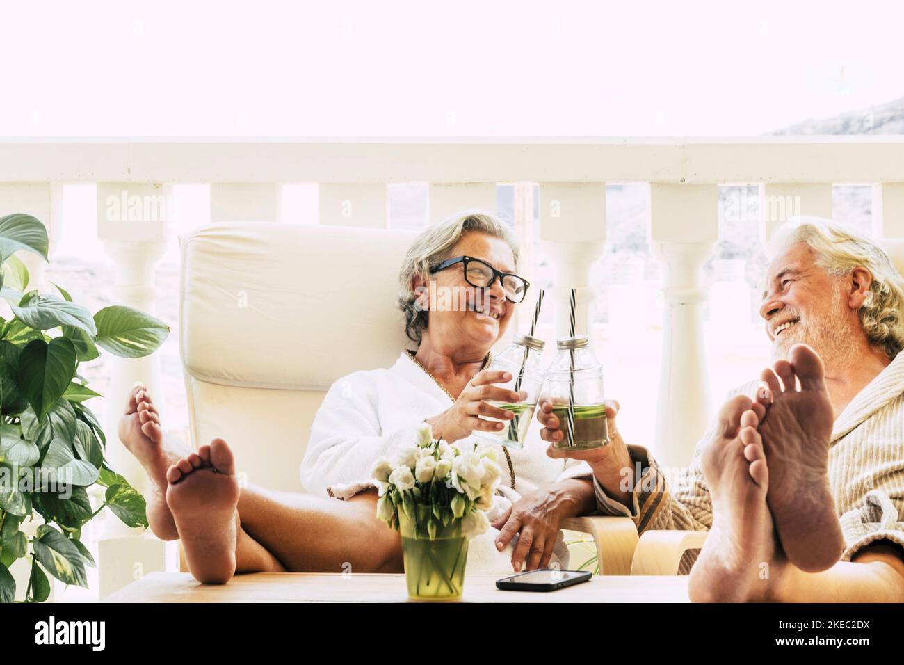 cute couple of seniors in a resort or beauty treatment at home or in a hotel having fun drinking a cocktail together and clinking it Stock Photo