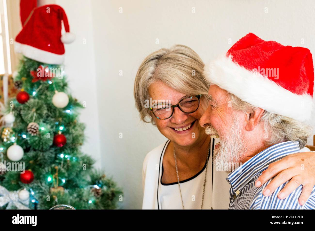couple of two old people pensioners having fun and laughing together at home with a christmas tree at the background and with the mature man wearing christmas cap or hat Stock Photo