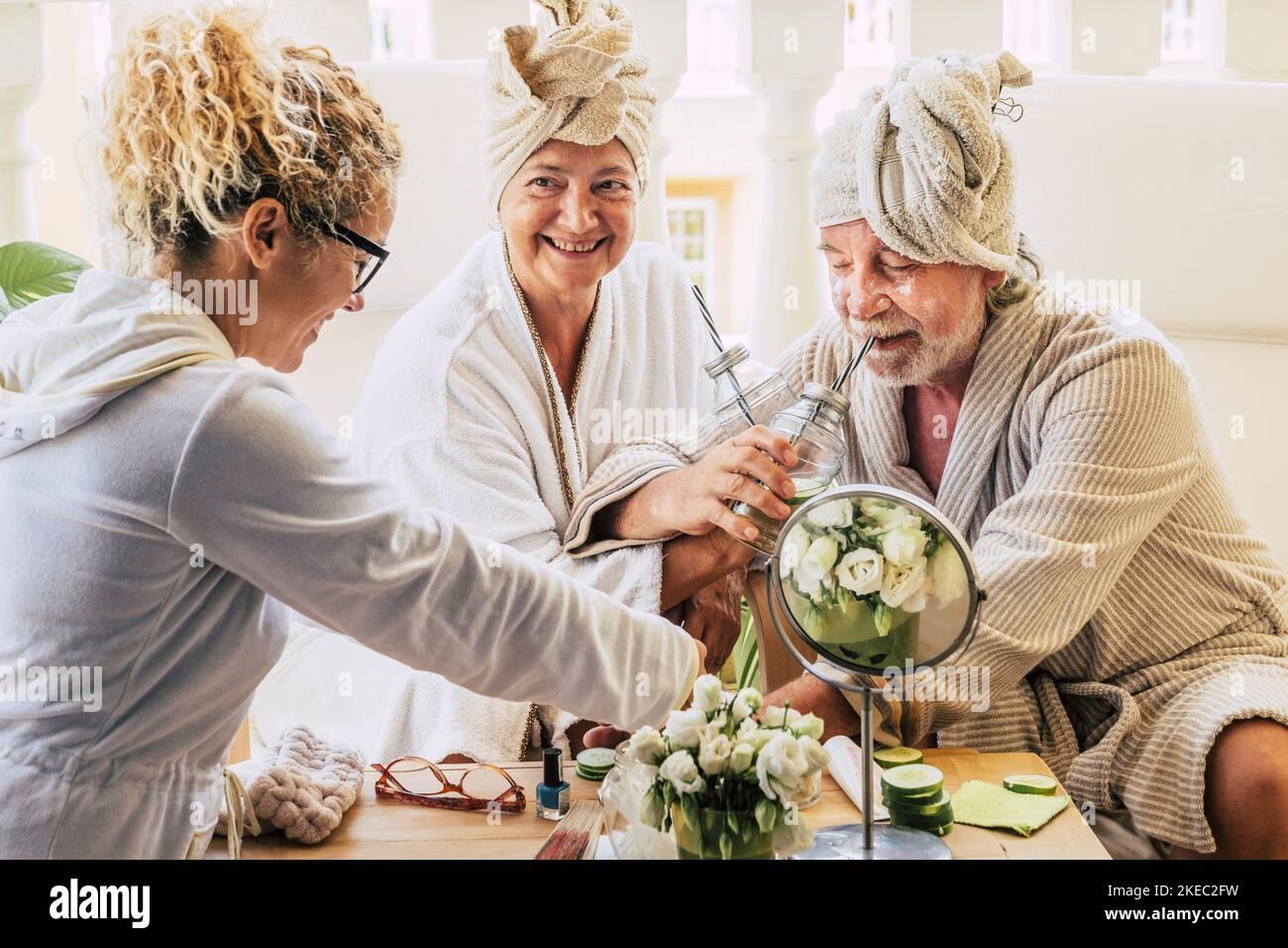 couple of two seniors enjoying a spa and massage traetment together with an assistance helping them - drinking cocktails and having fun smiling Stock Photo