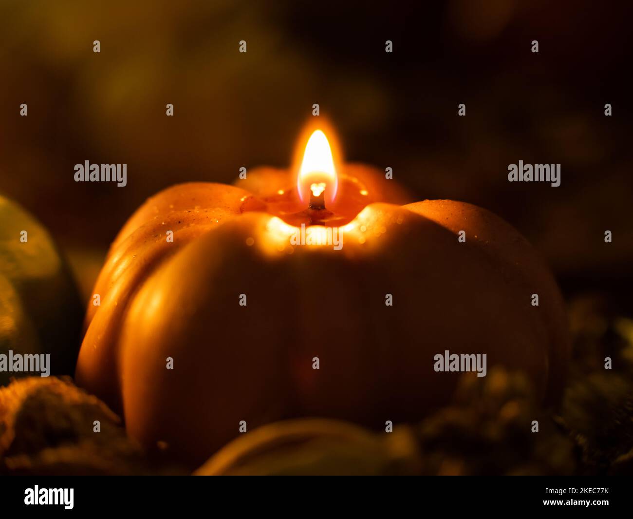 Pumpkin shape candle in a dark setting. Fire is glowing and making a warm atmosphere. Beautiful autumn decoration in the room. Close-up of a candle. Stock Photo