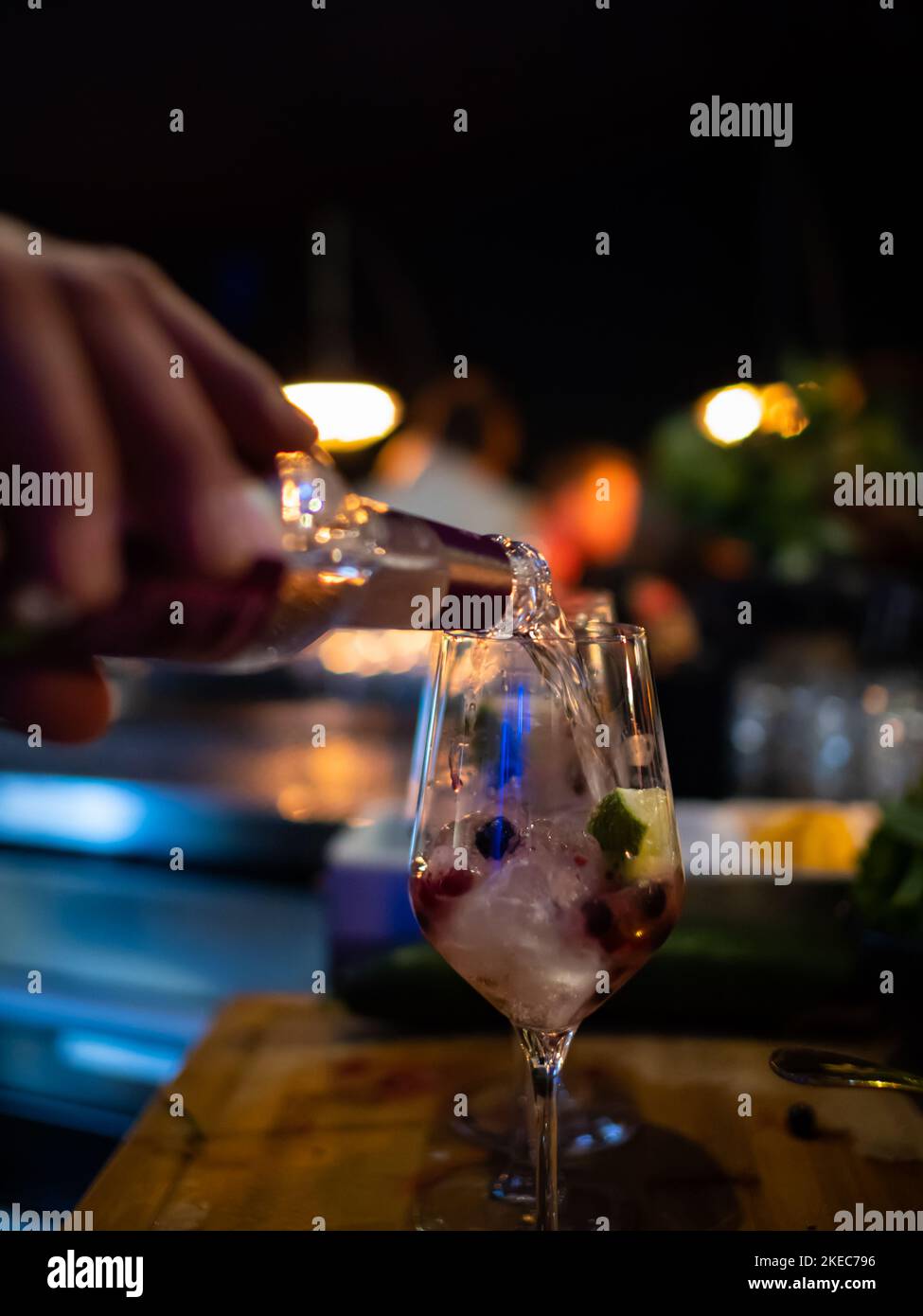 Mixing a cocktail at a bar. The bartender is pouring in a drink with wild berries and ice cubes. Close-up of the glass on the wooden table. Stock Photo