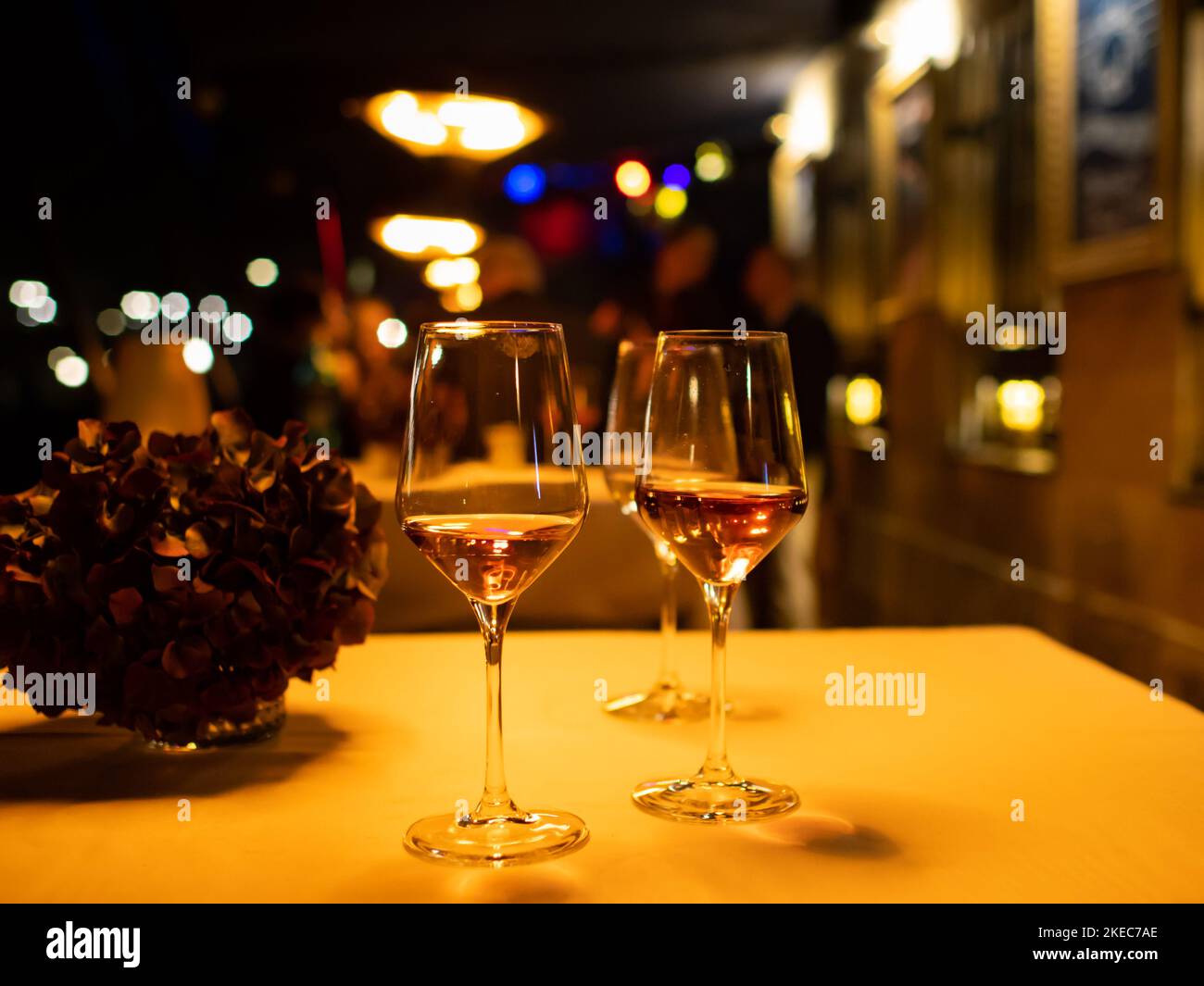 Two glasses with sparkling wine standing on a table. Warm tungsten light is illuminating the scene. Lipstick is on the glass of the alcoholic beverage Stock Photo