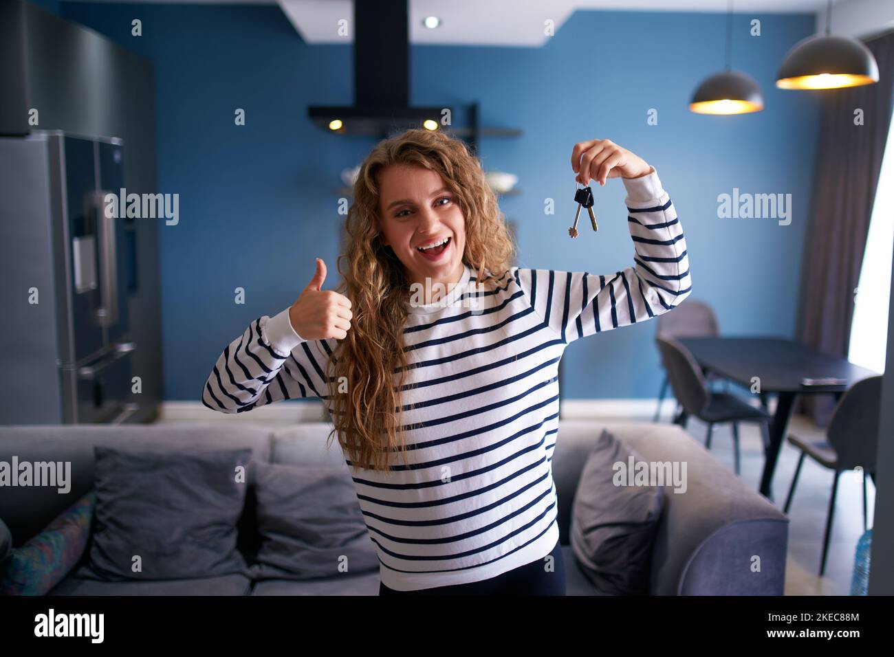 Happy woman showing new house or apartment keys to camera in modern interior. Female tenant renter with new home keys moving to tenancy. Lady Stock Photo