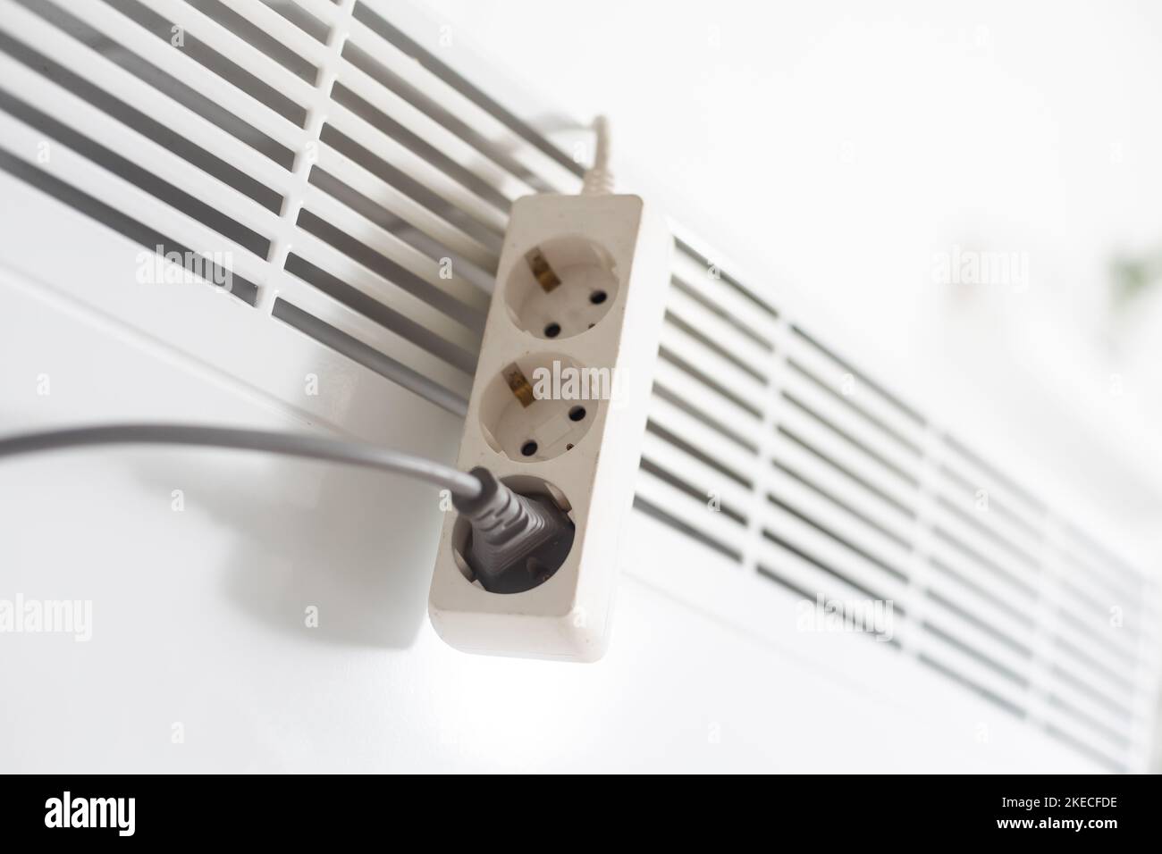 Electric heater plug inserted into extension cord. White radiator for