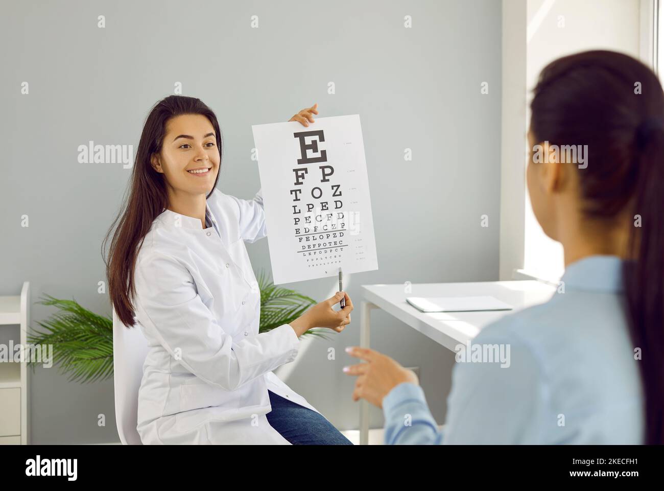 Ophthalmologist checks woman's eyesight by pointing to small letters on chart for vision test. Stock Photo
