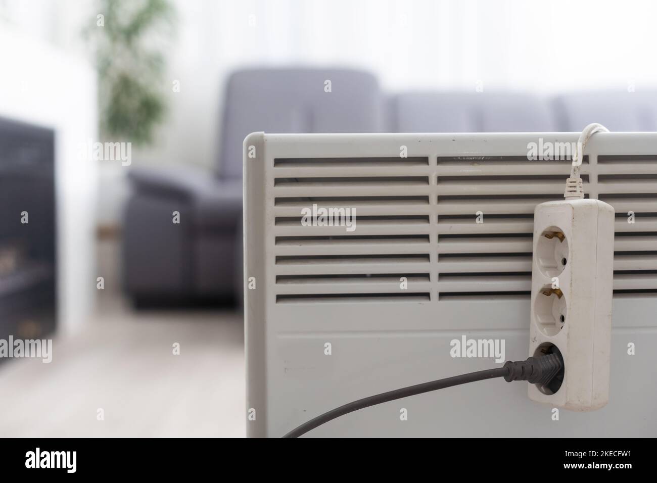 Electric heater plug inserted into extension cord. White radiator for home and office. House