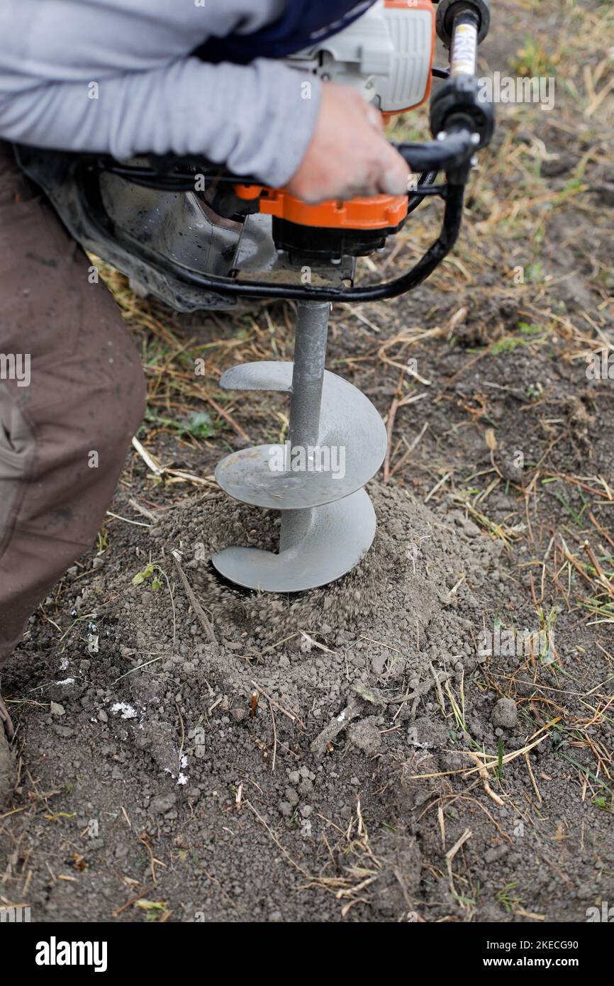 Shallow depth of field (selective focus) details with a man using a hand held earth hole drilling machine during a November tree planting on muddy soi Stock Photo