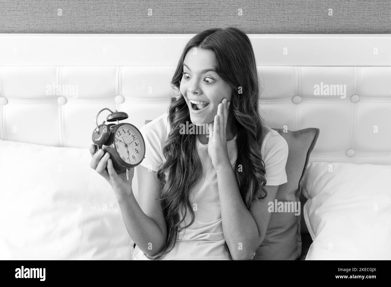 Shocked child look at alarm clock on waking in morning, shock Stock Photo